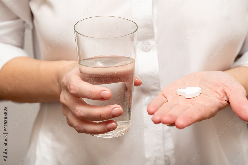 A young girl holds vitamins and a glass of water in her hands.