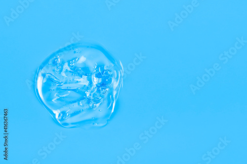 Clear transparent liquid gel drop or smear isolated on blue background. Top view. Virus protection or cosmetics concept. Serum texture. Banner with copy space