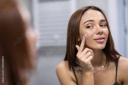 Attractive woman putting anti-aging cream on her face in bathroom