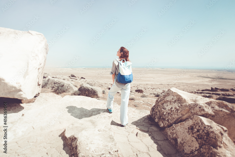 young woman traveler climbed to the top and looks at the beautiful landscape. She is wearing a blue backpack.
