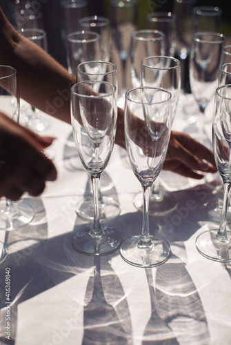 The arranging hand of empty glasses on a white table with a shadow. Catering set with empty glasses for luxury event.