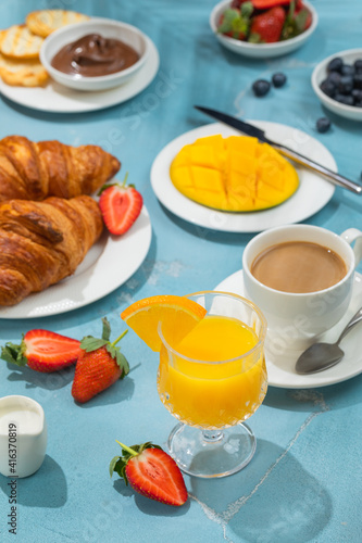 Luxury sunny continental breakfast on blue concrete background table with tropical plants shadows