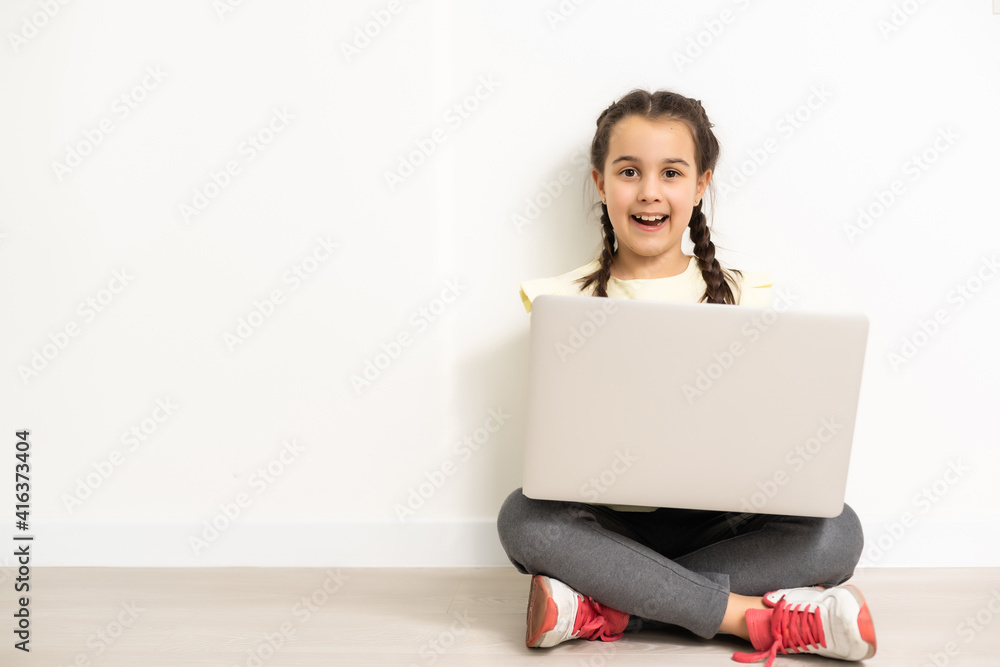 Full length little girl sitting on the floor, laptop computer screen, isolated over white Full length little girl sitting on the floor, laptop computer screen, isolated over white