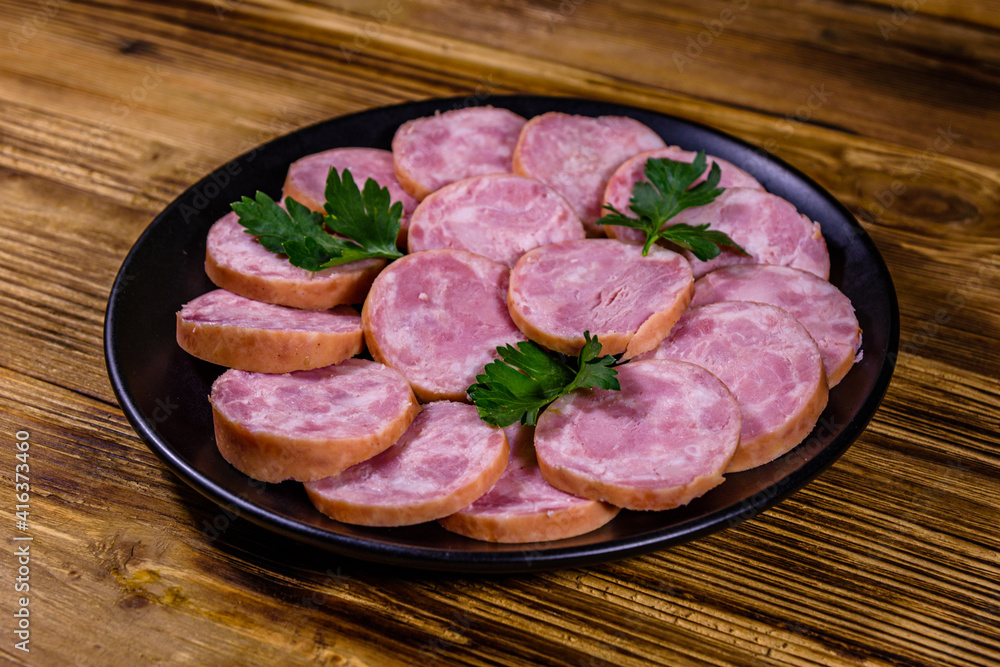 Black plate with sliced sausage on a wooden table Black plate with sliced sausage on a wooden table