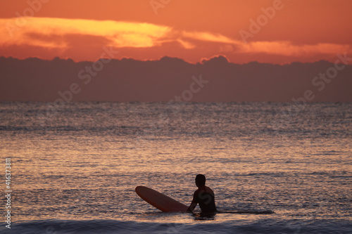Surfer sitzt auf seinem Brett und wartet auf den Sonnenaufgang