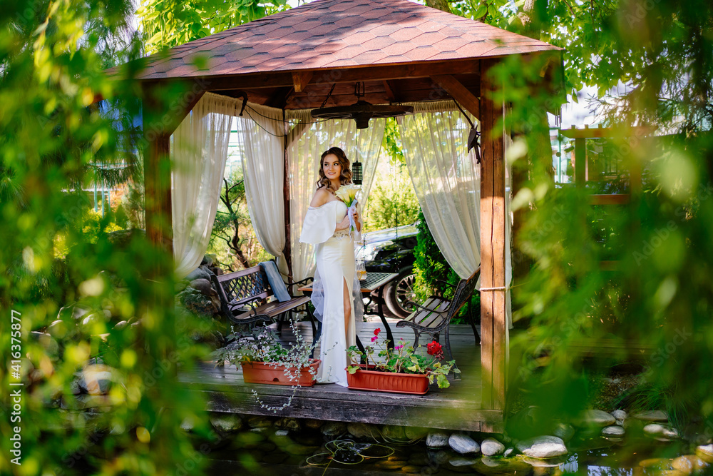 bride with long curls with bouquet of lilies kalla in a gazebo in a summer park