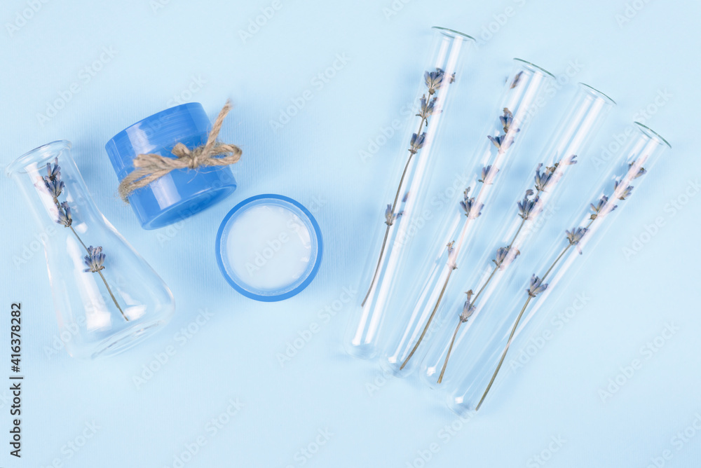 Test tubes and jars with natural cosmetics from lavender on a blue background. Lavender cream. Test tubes and jars with natural cosmetics from lavender on a blue background. Lavender cream.