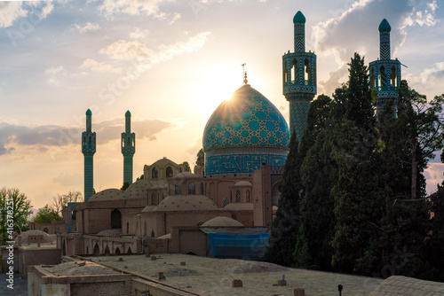 Sun sets behind the blue dome of Vali Shrine mosque viewed from a rooftop. On the rooftop of Shah Nematollah Vali Shrine, Mahan, Iran.