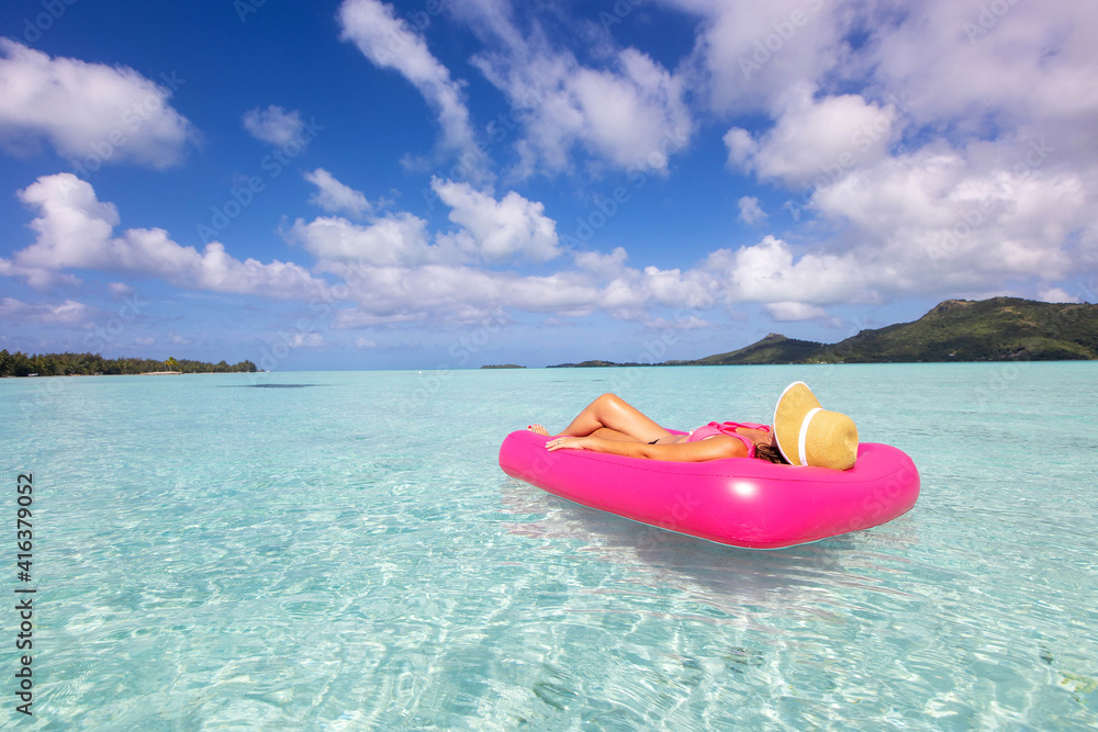 Woman on pink inflatable mattress over tropical turquoise ocean water