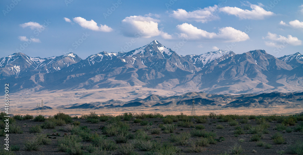 Tall mountains with snow on top rise above the Iranian desert. Majestic four-thousanders in a soft haze on a sunny day in ancient Persia.
