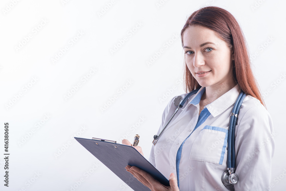Portrait of a young female doctor in a white uniform with a folder and a pen in hands in the studio on a white background with copyspace
