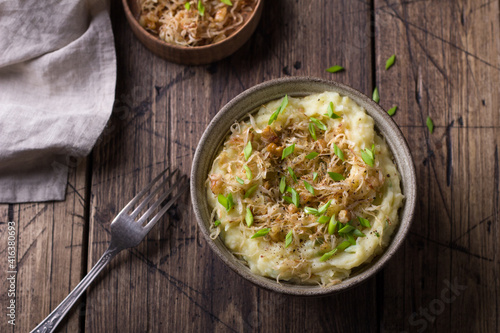 Traditional Irish dish colcannon, mashed potatoes with cabbage and green onions, on top of crispy fried cabbage topping with nuts and spices on a wooden table
