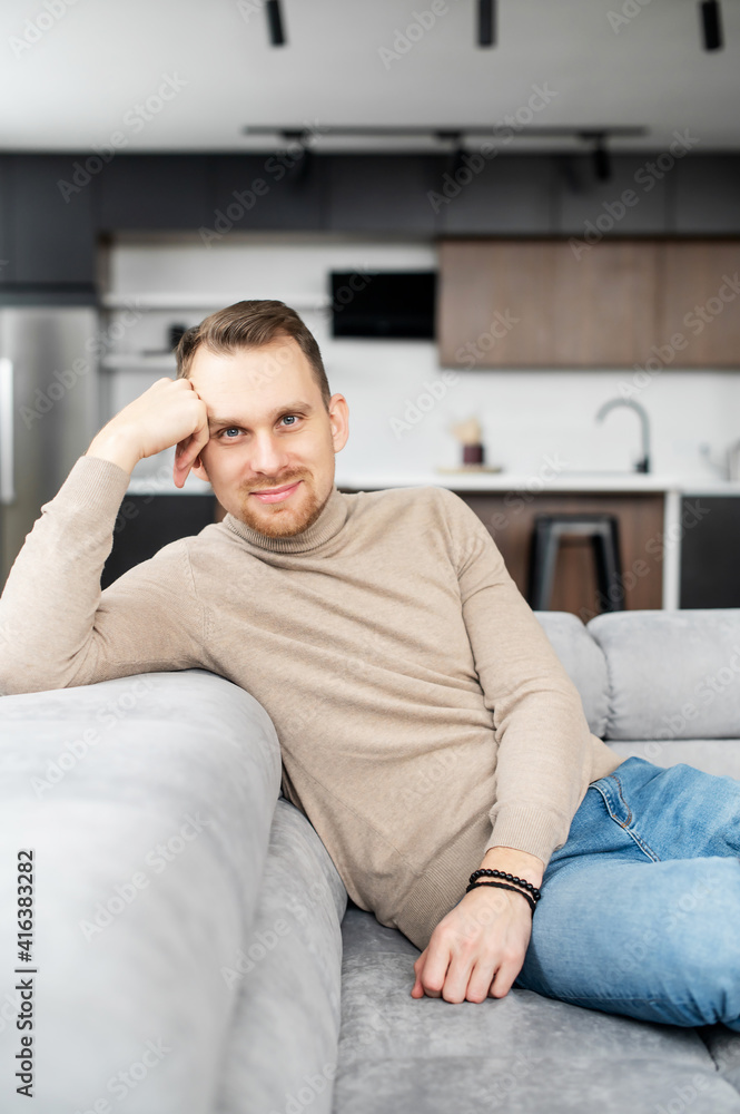 Confident and slender man with light brown hair, grey eyes and short neat bristle, sitting, head resting on one hand and looking at camera, flirting, friendly, posing, wearing beige sweater and jeans Confident and slender man with light brown hair, grey eyes and short neat bristle, sitting, head resting on one hand and looking at camera, flirting, friendly, posing, wearing beige sweater and jeans