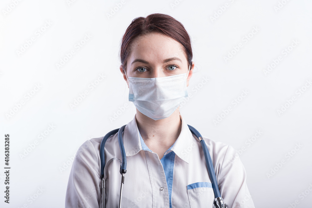 Portrait of a female doctor in a white uniform with a medical mask on her face in the studio on a white background Portrait of a female doctor in a white uniform with a medical mask on her face in the studio on a white background