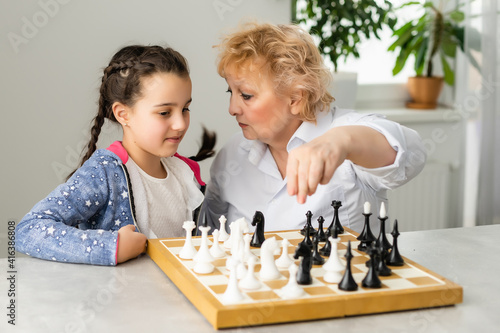 Young girl playing chess with grandmother together at home