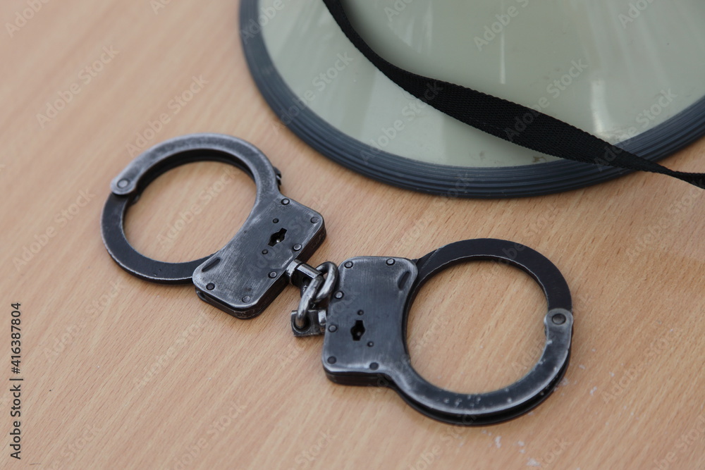 Closed handcuffs and police helmet on wooden table closeup, policeman equipment Closed handcuffs and police helmet on wooden table closeup, policeman equipment