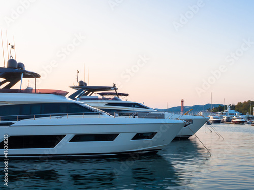Two white yachts are moored in a calm sea with other ships and shore visible in the distance © jockermax3d