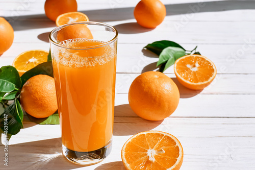 Ripe bio oranges and a glass of fresh squeezed orange juice on white wooden background. Organic Sicilian oranges.