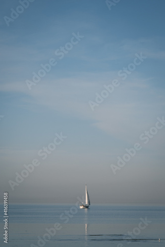 white sailing ship floats on the sea and the water is very still