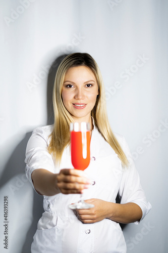 Beautiful blonde woman in white shirt is holding glass with red drink