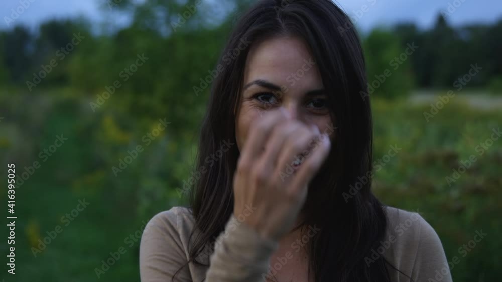 Young adult woman smiling towards camera brushes hair outdoors with green foliage backgroud Young adult woman smiling towards camera brushes hair outdoors with green foliage backgroud