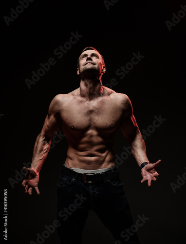 Handsome sexy man with muscular body, showing a welcome gesture, standing on a black background. Sports, bodybuilding motivation. Dark studio shot with copy space portrait