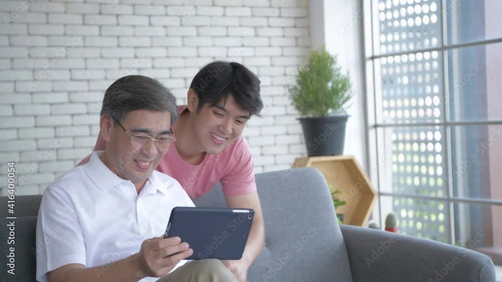 Family concept of 4k Resolution. Asian son and dad are having fun playing tablets in the living room. Family concept of 4k Resolution. Asian son and dad are having fun playing tablets in the living room.