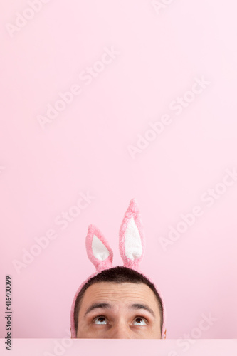 A man on a pink background, with pink rabbit ears on his head. Concept for Easter celebrations, emotions on face. Copy space.