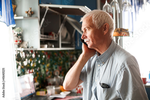senior grandfather talking with phone near window at home. elderly man sad. grandfather chatting with relatives or grandchildren. Soft focus