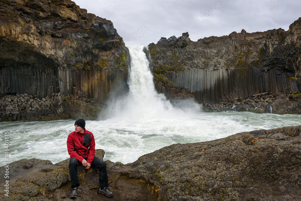 Tourist sits at the Aldeyjarfoss waterfall in northern Iceland