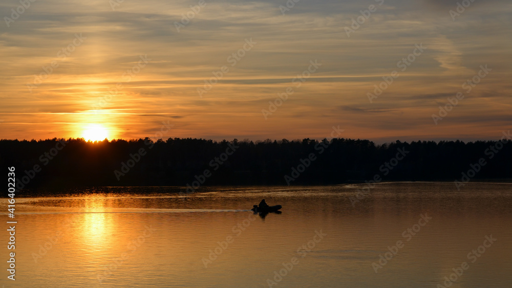 Orange sunset over the lake with silhouette of fisherman boat. Selective focus.