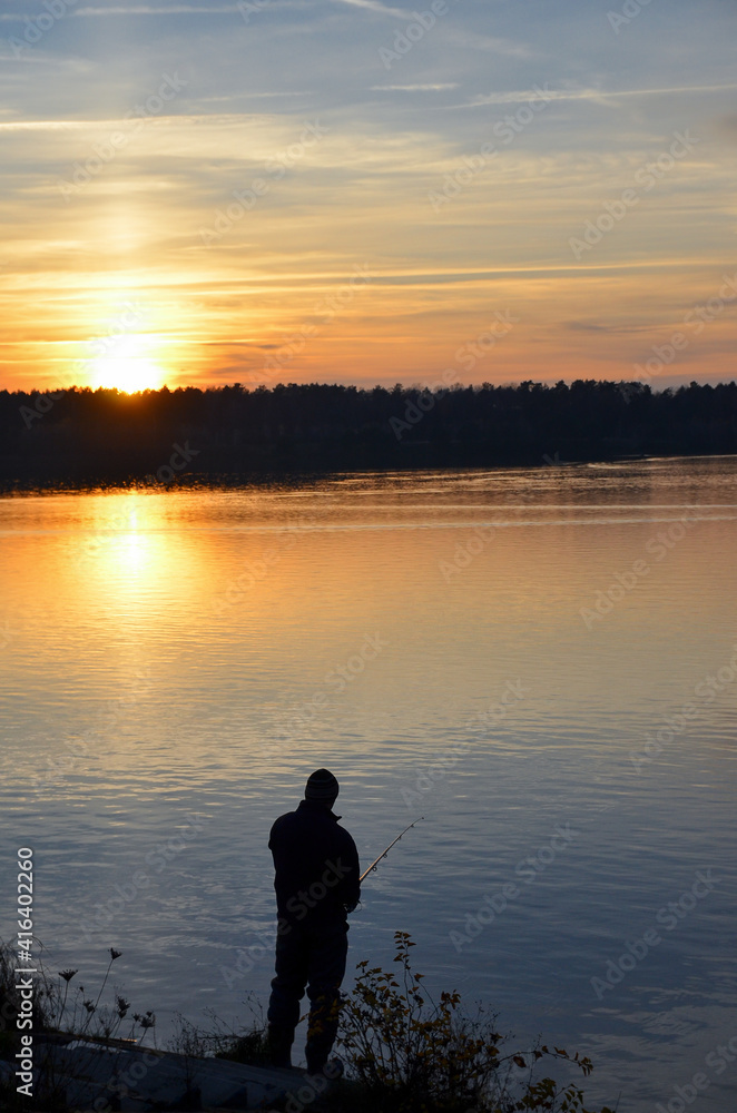 Silhouette of fisherman on the background of orange sunset over the lake. Selective focus.