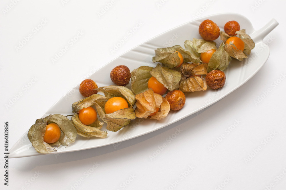 Golden Berry, Physalis or Cape Gooseberry - Healthy Tropical Yellow-Orange Fruit. Fresh and Dried Fruits on a white Plate shaped like a Banana Leaf. Golden Berry, Physalis or Cape Gooseberry - Healthy Tropical Yellow-Orange Fruit. Fresh and Dried Fruits on a white Plate shaped like a Banana Leaf.