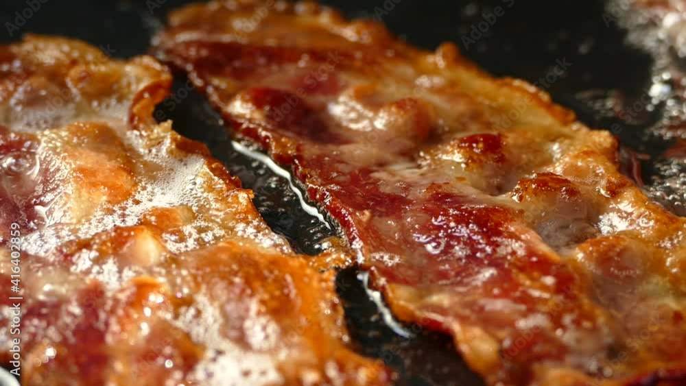 Fry the bacon in a pan. A slice of pork bacon is prepared in its own fat. Layer of meat and lard. Close up in the kitchen. Fry the bacon in a pan. A slice of pork bacon is prepared in its own fat. Layer of meat and lard. Close up in the kitchen.
