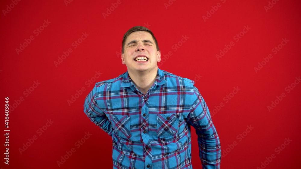 A young man has a backache and is holding it in his hands. Shooting on a red background. A young man has a backache and is holding it in his hands. Shooting on a red background.