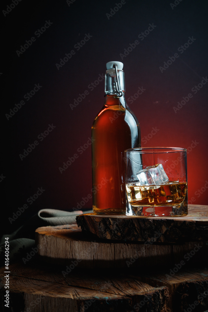 A glass of alcohol near a bottle. Old whiskey bottle on black wooden table. Drinks on a dark blurred background. A glass of alcohol near a bottle. Old whiskey bottle on black wooden table. Drinks on a dark blurred background.