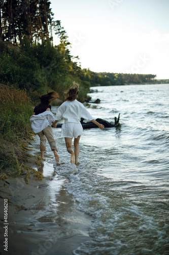 two young women hold hands and run barefoot along the beach at sunset. two girls run away
