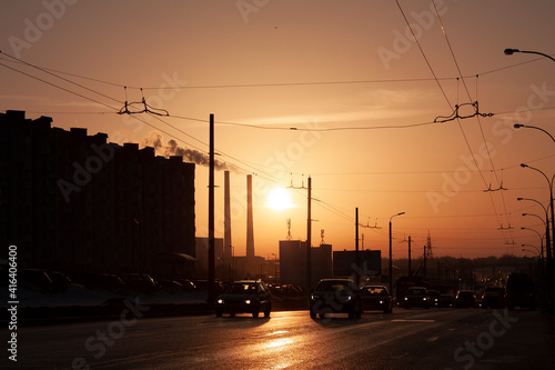 Horizontal dark cityscape photo of an urban skyline with a silhouettes of cars on the road during champagne colour winter sunset 