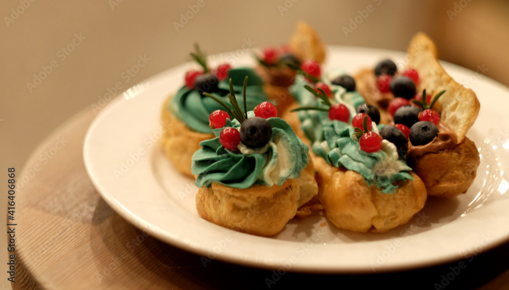 Tasty French eclairs with icing, cream, fresh berries and sugar decor elements.