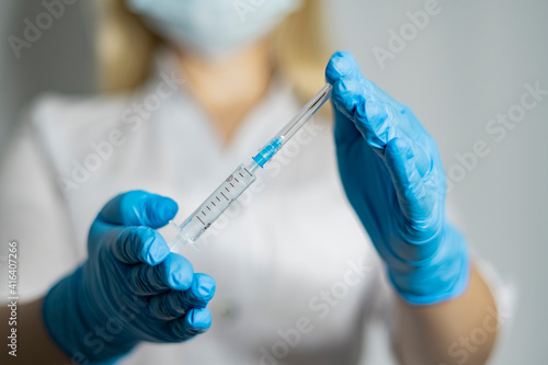 Female doctor with blue medical gloves holds a syringe