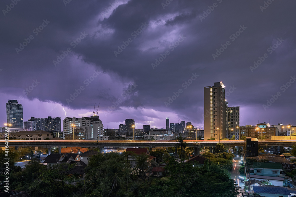 City landscape lightning storm behind clouds at night and highway light trails