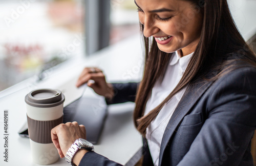 Portrait of smiling businesswoman sitting and looking at her smartwatch.