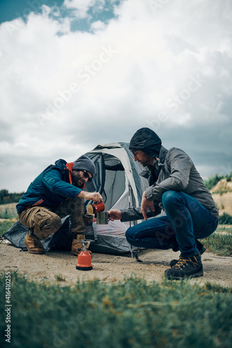 Two campers crouching by the tent and preparing coffee. © chika_milan