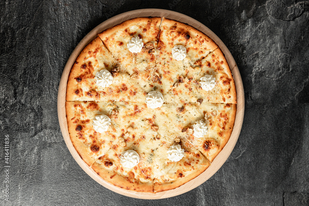 Hot tasty traditional italian pizza with salami, meat, cheese, tomatoes greens on a dark background Hot tasty traditional italian pizza with salami, meat, cheese, tomatoes greens on a dark background