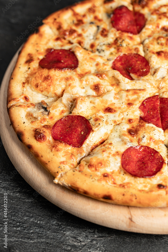 Hot tasty traditional italian pizza with salami, meat, cheese, tomatoes greens on a dark background Hot tasty traditional italian pizza with salami, meat, cheese, tomatoes greens on a dark background
