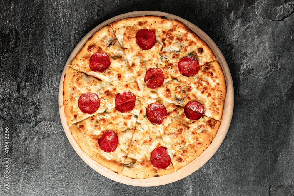 Hot tasty traditional italian pizza with salami, meat, cheese, tomatoes greens on a dark background Hot tasty traditional italian pizza with salami, meat, cheese, tomatoes greens on a dark background