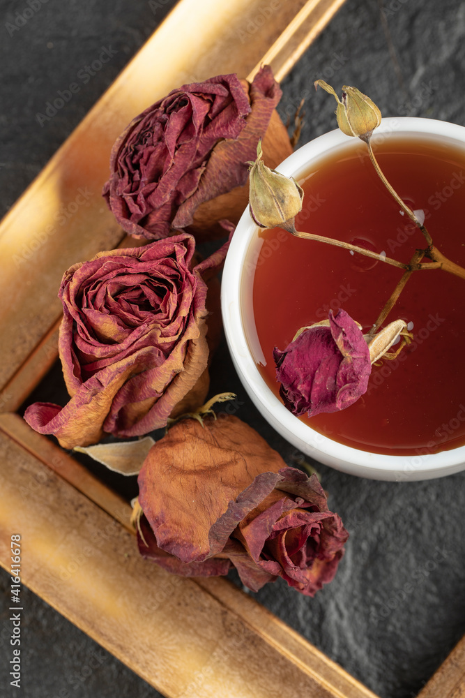 A cup of tea with dried rose and frame on a black background