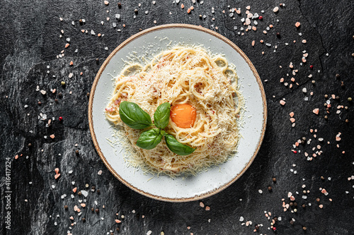 Pasta Carbonara on white plate with parmesan and yolk on dark marble background