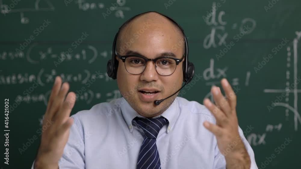 Indian young teacher man sitting wearing headset teaching online video conference live stream by laptop. Asian teacher teaching mathematics class webinar online for students learning. Indian young teacher man sitting wearing headset teaching online video conference live stream by laptop. Asian teacher teaching mathematics class webinar online for students learning.
