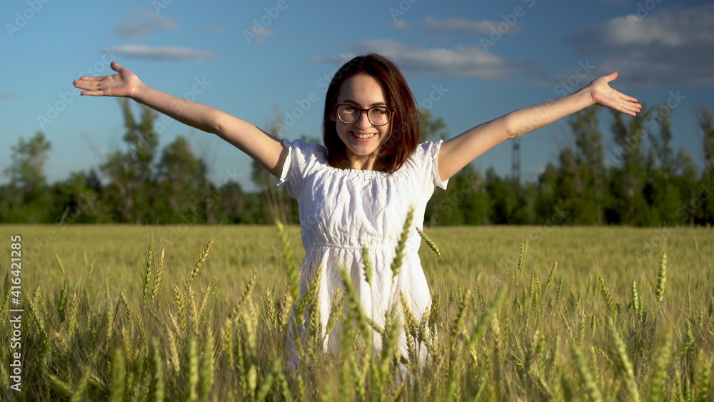 A young woman in a white dress jumps out of a green wheat field. The girl suddenly appears and smiles. A young woman in a white dress jumps out of a green wheat field. The girl suddenly appears and smiles.